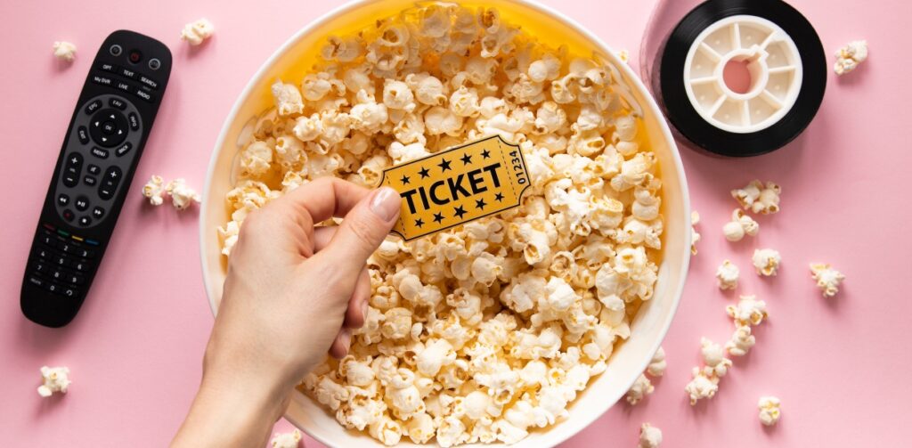 Mão em cima de balde de pipoca com ingresso, simbolizando como conseguir desconto no cinema