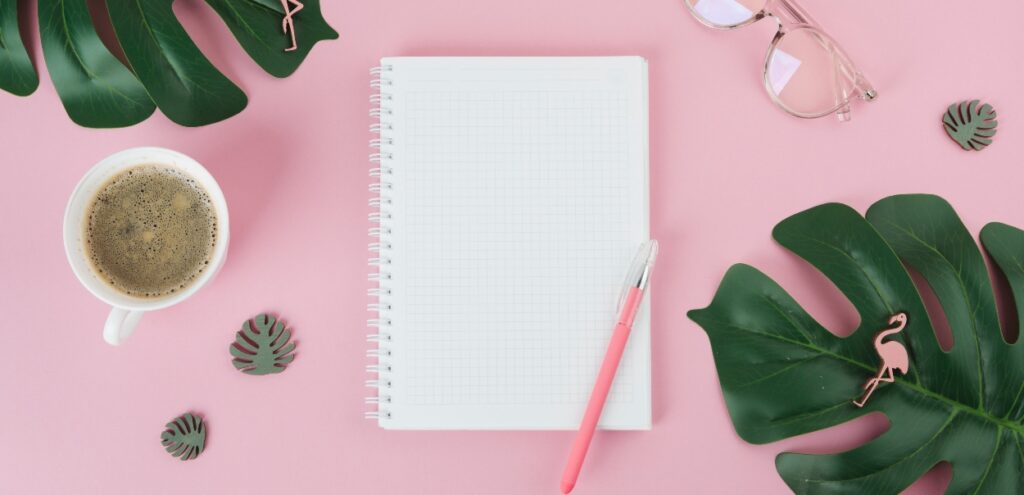 Caderno em branco e uma caneta rosa, representando a pesquisa de satisfação no ambiente de trabalho.