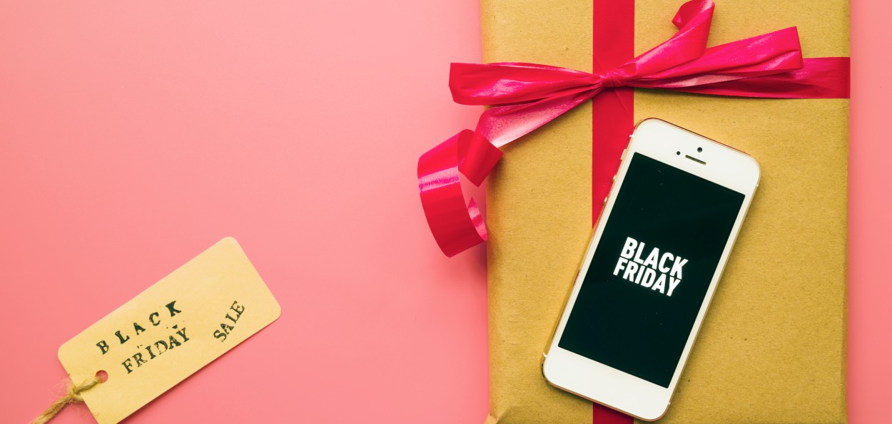Imagem de um presente em um fundo rosa e um celular escrito "Black Friday" para representar a data.
