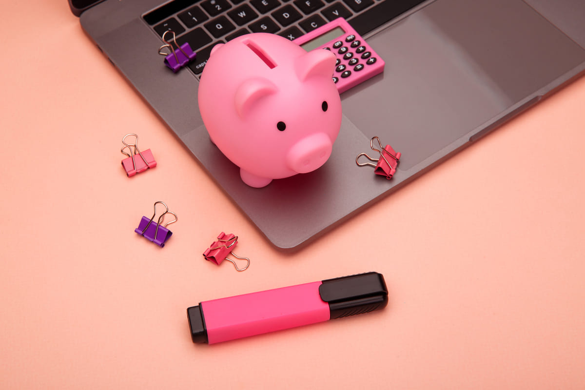 Cofrinho de porquinho e calculadora sobre notebook, representando o bem-estar financeiro.